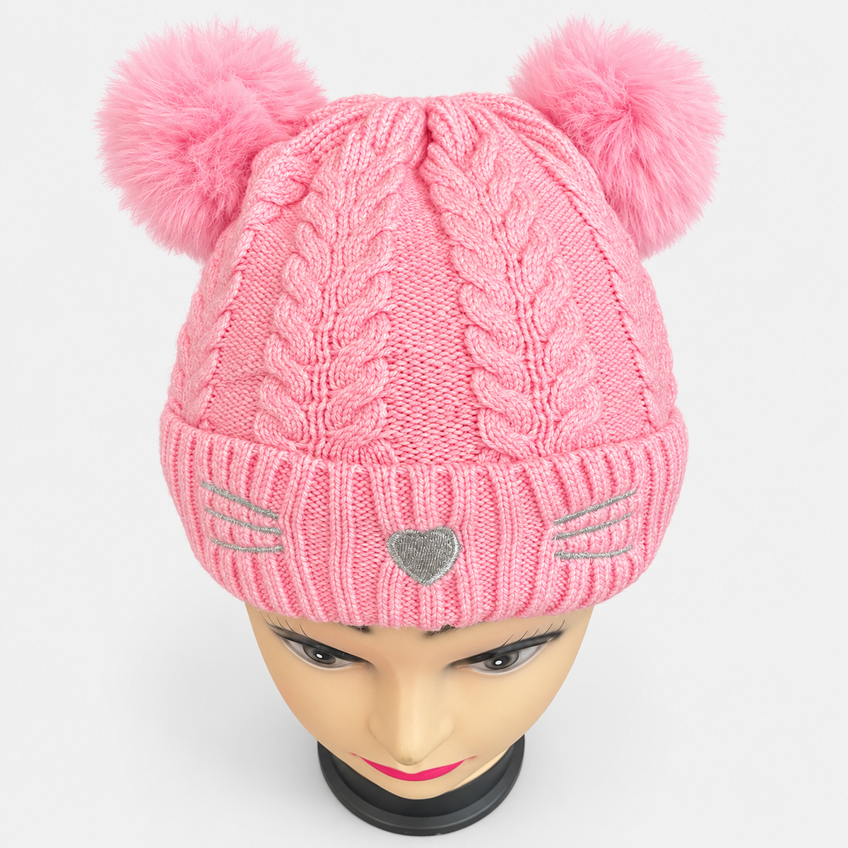 Pink double pom-pom cat-face cable knit beanie worn on a mannequin, showing the cable knit, folded cuff and silver embroidery